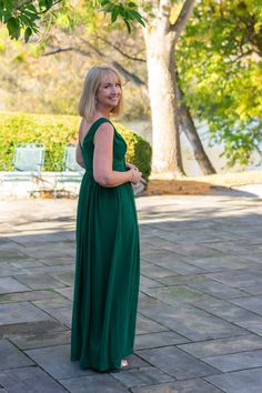 a woman in a long green dress standing on a brick walkway with trees behind her