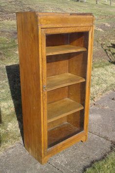 an old wooden bookcase sitting on the side of a road in front of a grassy field