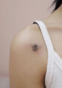 a woman's shoulder with a small tattoo of a bee on the left side