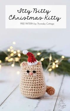 a crocheted christmas kitty sitting on top of a wooden table with lights in the background