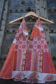 an orange and pink dress hanging on a wooden hanger in front of a metal door