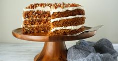 a carrot cake with white frosting and walnuts on a wooden platter next to a knife