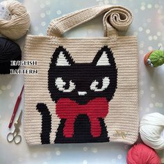 a crocheted bag with a black cat on it next to yarn and scissors