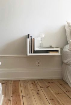 there is a shelf with books on it next to a bed and nightstand in the corner