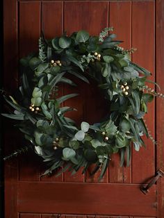 a green wreath hanging on the side of a wooden door with greenery and berries