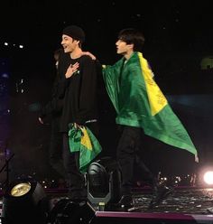 two young men are walking on stage with green and yellow flags in their hands while one man is holding his arms around the other