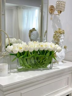 a vase filled with white tulips sitting on top of a table next to a mirror