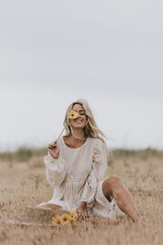 a woman sitting in a field with sunflowers and holding a flower up to her face