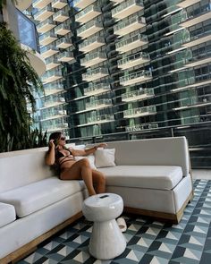 a woman sitting on top of a white couch next to a tall building with balconies