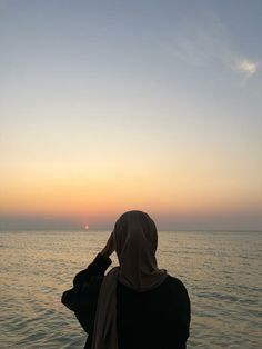 a woman sitting on the edge of a boat looking out at the ocean during sunset