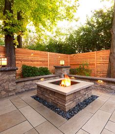 an outdoor fire pit surrounded by stone walls and wooden fence with trees in the background