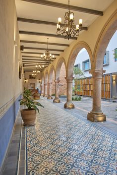 an ornate hallway with blue and white tiles on the floor, chandeliers and potted plants