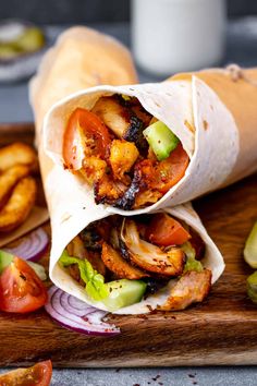 two wraps filled with meat and vegetables sitting on a cutting board next to onion rings