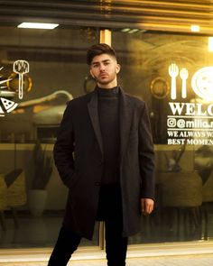 a man standing in front of a glass door with his hands in his pockets and looking at the camera