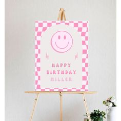 a pink happy birthday card sitting on top of a easel next to a potted plant