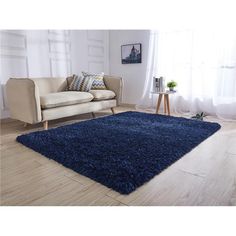 a living room with a couch, chair and blue rug on the hardwood floor in front of a window