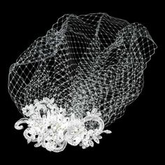 a white veil with flowers on it and some netting over the top, against a black background