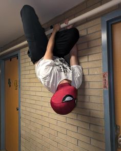 a man hanging upside down on a wall with his hands in the air and wearing a red hat