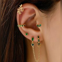 a close up of a person's ear with green and gold jewelry on it