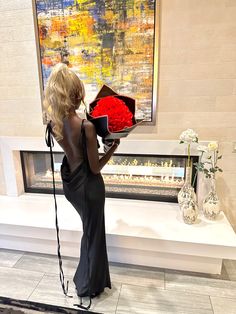 a woman in a black dress is holding a red bouquet and looking at it on the wall