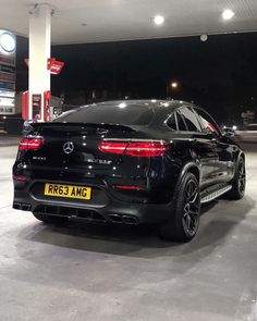 the rear end of a black mercedes suv parked at a gas station with its lights on