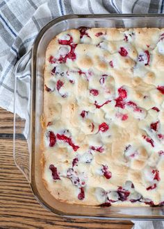 a casserole dish filled with cranberries and white sauce on top of a wooden table