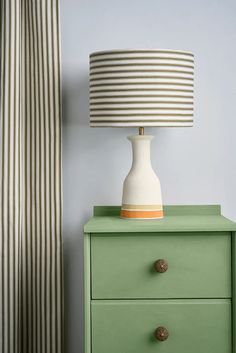 a green dresser with a white and orange lamp on it next to a striped curtain