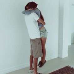 a man and woman standing next to each other in front of a wall with their arms around each other