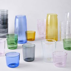 many different colored glass cups are arranged in a circle on a white surface, one is empty and the other is half full