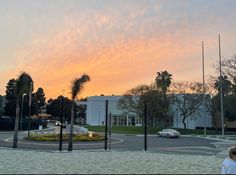 the sun is setting behind some palm trees in front of a building with cars parked on the street