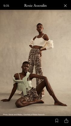 two women pose in front of a wall wearing patterned pants and cropped tops, one with her leg up on the ground