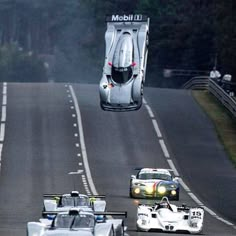 three race cars racing on the road with trees in the backgrounds