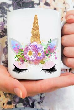 a person holding a coffee mug with an unicorn's face on it and flowers