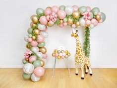 a giraffe standing in front of a balloon arch with flowers and balloons on it