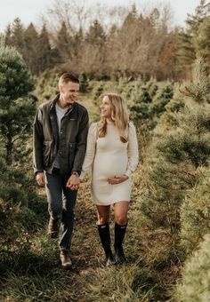 a pregnant couple holding hands and walking through a christmas tree farm