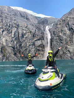 two people on jet skis in front of a waterfall with mountains and blue water