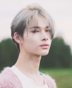 a young man with grey hair and piercings on his ear wearing a pink sweater