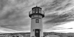 a black and white photo of a lighthouse in the middle of some rocks with a cloudy sky behind it