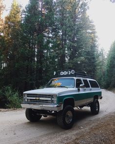 a green and white truck parked on the side of a dirt road next to trees