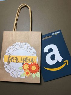 a brown paper bag with an amazon gift card next to it and a blue shopping bag that says for you