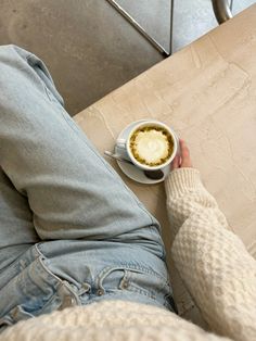 a person sitting at a table with a cup of coffee in their hand and the bottom half of their leg up