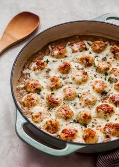 a casserole dish with meatballs and cheese in it next to a wooden spoon