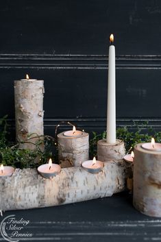 a group of white candles sitting on top of a wooden table next to some logs