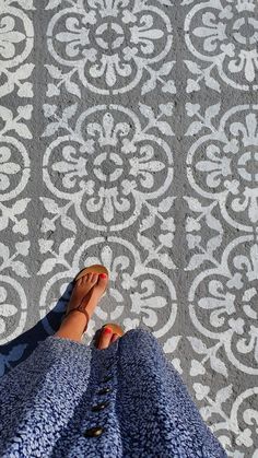 a woman's feet with red nail polish standing in front of a patterned wall