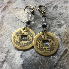 COIN EARRINGS These coin earrings are hand-made from a brass replica of an old Chinese "cash" coin used in China and East Asia, from the 4th century BC until the 20th century AD, characterized by their round outer shape and a square center hole (方穿, fāng chuān). Apart from their attractive shape, these coins conjure up human transactions over the centuries, the exchange of spices, silk and tea...they call to the past... to the time of Shanghai Lily in the 1930's.... The focal bead is a clear faceted Czech crystal bead complemented by two faceted black bicone Czech beads. CLOSURE Lever Back - Antiqued Bronze - Nickel Free  GIFT These coin earrings are a thoughtful gift for those who have an interest in Asia.  They convey good fortune and friendship and are a perfect gift for those who pract Asian Jewelry, December Birthday, Zen Meditation, Earrings Crystal, Czech Crystal, Czech Beads