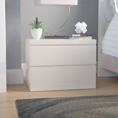 a white nightstand with a lamp on top of it next to a bed and rug