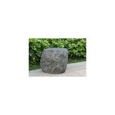 a large rock sitting on top of a sidewalk next to a lush green hedge covered in leaves