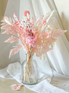 a glass vase filled with pink flowers on top of a white cloth covered tablecloth