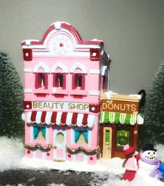 a pink toy store with snow on the ground next to it and a small snowman standing in front of it