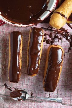 three chocolate covered donuts sitting on top of a table next to a bowl of dipping sauce